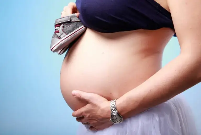 Photo de grossesse avec petite chaussures sur fond bleu et main sur le ventre